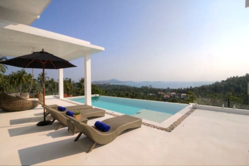 Piscine à débordement de la Villa Indigo Samui surplombant Ko Samui avec transats, parasol noir et vue sur les montagnes au coucher de soleil
