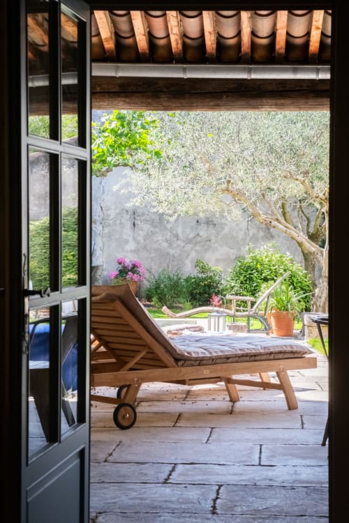 Chaise longue en bois sur terrasse en pierre au gîte Le Jardin Secret à Grignan, France, vue sur un jardin luxuriant fleuri