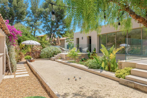 Le jardin paisible de la cour de pétanque de la Villa Luna avec ses plantes luxuriantes, pergola ombragée et terrasse moderne à Jc Conciergerie, Bandol