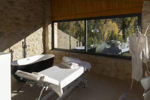 Modern spa bathroom at El Batán Hotel with black freestanding tub, treatment bed, and countryside views in Castillo de