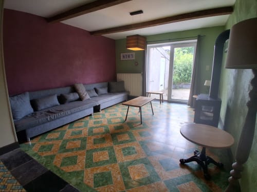 Espace lounge moderne au gîte Les Trois Voisins à Bourseigne-Vieille avec canapé gris, carrelage motifs et murs verts.