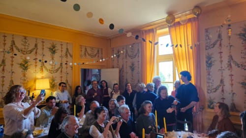 Guests gathered in warmly decorated dining room at Château de Vaux Morvan with yellow curtains and botanical wall decor