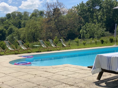 Resort pool at Château de Vaux Morvan with lounge chairs, floats, and forested backdrop in Étang sur Arroux