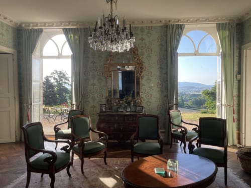 Elegant parlor at Château de Vaux Morvan with green upholstered chairs, crystal chandelier, and panoramic river valley views