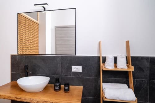 Bagno moderno a Domo Cadò con lavabo bianco a coppa, vanity in legno, rivestimento in piastrelle scure e scala portasciugamani
