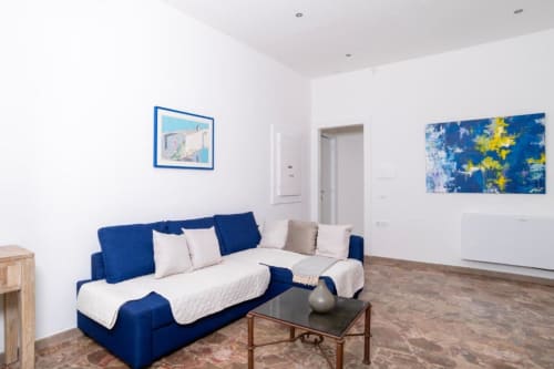 Camera deluxe al Domo Cadò a Berchidda con divano blu, biancheria bianca, arte moderna e vista sul giardino