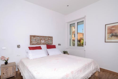 Camera da letto di lusso luminosa a Domo Cadò a Berchidda con letto matrimoniale, cuscini rossi, vista giardino e servizi moderni