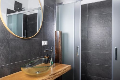 Moderno bagno al Domo Cadò con piastrelle in ardesia scura, mobile in legno, lavabo da appoggio, specchio tondo e cabina doccia
