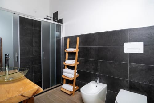 Bagno moderno a Domo Cadò BnB a Berchidda con piastrelle nere, cabina doccia in vetro, bidet bianco e asciugamani in legno