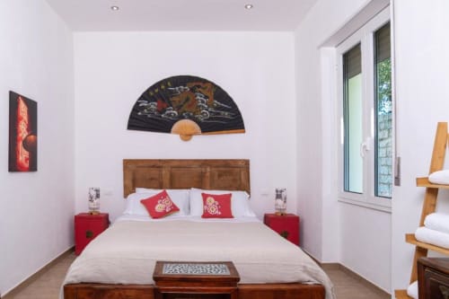 Camera moderna a Domo Cadò con letto in legno, comodini rossi, arte asiatica e vista sulla corte