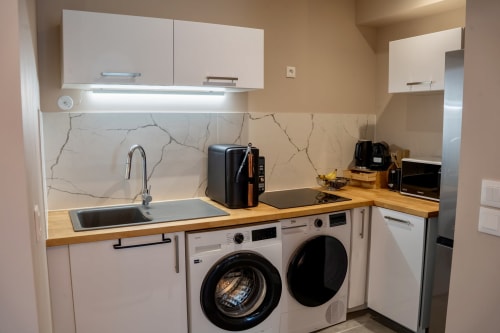 Modern kitchen in Castres apartment with white cabinets, wood countertops, marble backsplash, sink, and integrated
