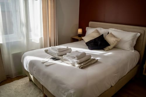 Spacious bedroom in Le 1 Péraudel Suite with cream bedding, fresh towels, dark accent wall, and garden view in Castres