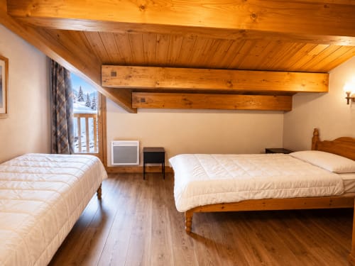 Chambre spacieuse aux Étoiles de la Plagne avec deux lits, poutres apparentes, parquet et vue montagne