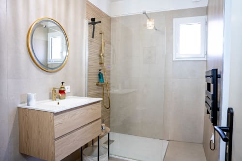 Salle de bains moderne avec vanité en bois, miroir rond doré, douche à l'italienne et carrelage beige à la suite luxe Le Mas De La Clé D'Or