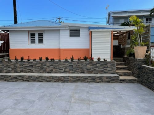 Bungalow Corail de la Résidence B&L Lagon à Sainte-Luce : façade corail et blanche, cour pavée, jardin tropical