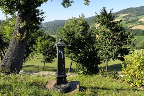 Monumento in marmo nero su piedistallo circondato da alberi, colline verdi ondulate e campi coltivati nella campagna toscana a Lodole Country