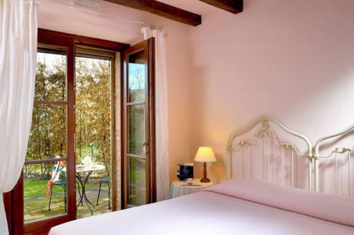 Luminosa camera da letto principale a Lodole Country House con letto ornato, porte color terracotta che si affacciano sul giardino a Monzuno, Italia