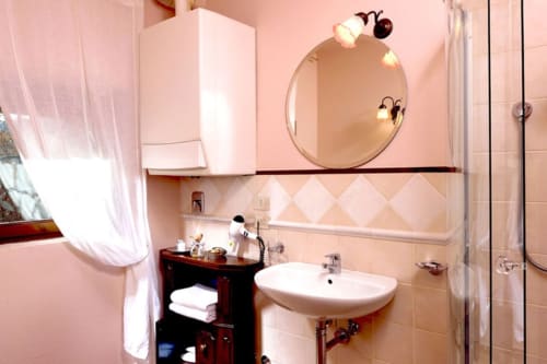Bagno rosa con specchio rotondo e lavabo della Lodole Country House B&B a Monzuno, Italia