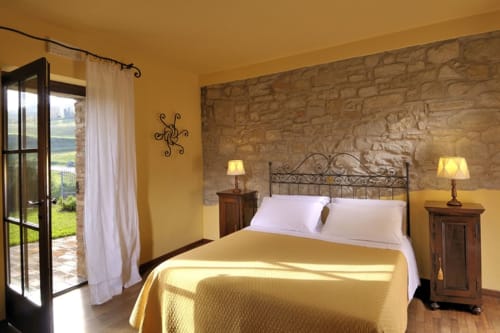 Luminosa camera superior a Lodole Country House a Monzuno con muro in pietra, letto in ferro battuto e vista sulla campagna
