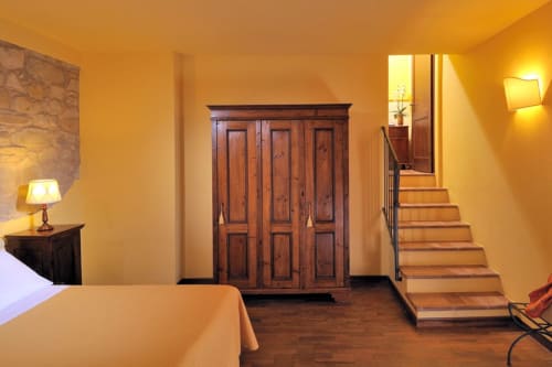 Camera calda e luminosa alla Lodole Country House con armadio in legno, letto, lampada e scale in pietra che salgono