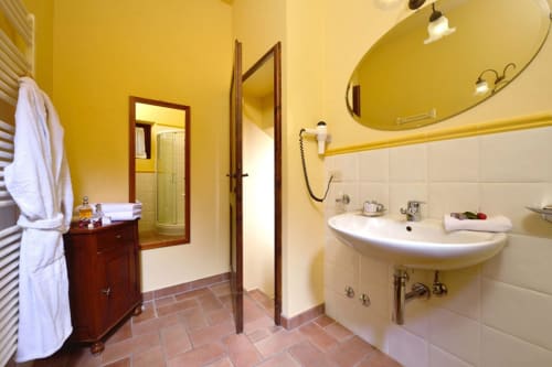 Luminoso bagno della Lodole Country House con pareti gialle, specchio curvo, lavabo bianco e pavimento in cotto