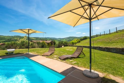 Area piscina della villa toscana con ombrelloni gialli, lettini e dolci colline verdi alla Lodole Country House, Monzuno Italia
