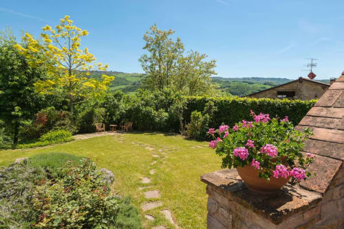 Giardino toscano di Lodole Country House con fiori rosa, prato, siepi e vista sulle colline