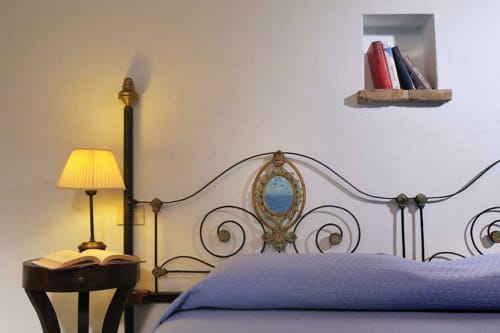 Camera elegante presso Lodole Country House con letto in ottone ornamentale, lampada da comodino e libri su scaffale a parete
