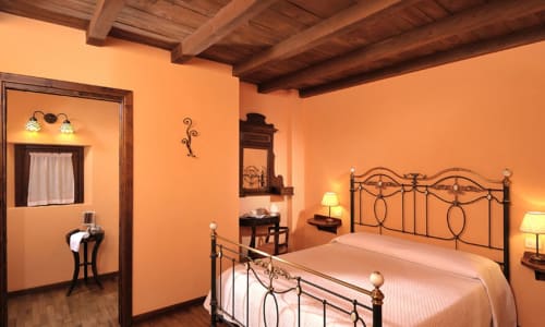 Camera Sunset Standard presso Lodole Country House, Monzuno: pareti color arancio caldo, soffitto con travi in legno, letto in ferro battuto ornamentale, bagno privato