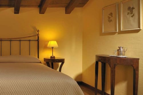 Camera accogliente a Lodole Country House con pareti gialle, letto in ferro, lampada da comodino e opere botaniche a Monzuno