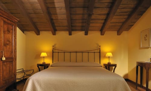 Camera standard accogliente alla Lodole Country House con travi a vista, pareti gialle, letto in ferro battuto e illuminazione calorosa.