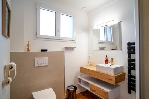 Salle de bains moderne du Mas De La Clé D'Or avec vasque en bois, lavabo blanc, miroir et grandes fenêtres lumineuses à Puget sur Argens