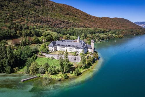 Château historique au bord d'un lac turquoise entouré de collines boisées à Trévignin, France