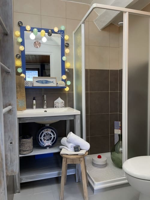 Salle de bains moderne de l'appartement La Jument Verte avec miroir lumineux, lavabo blanc, cabine de douche et décoration