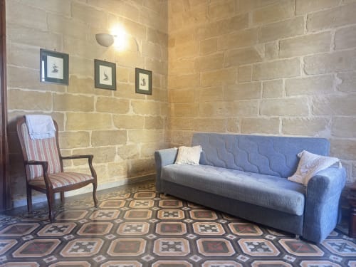 Lounge dell'appartamento Astricu a HABITARE Lecce con divano blu, sedia a righe e pavimento geometrico in setting di mattoni storici