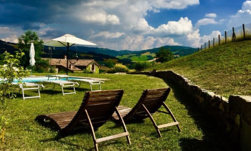 Area relax in campagna toscana con lettini, piscina e colline verdi ondulate presso Lodole Country House, Monzuno