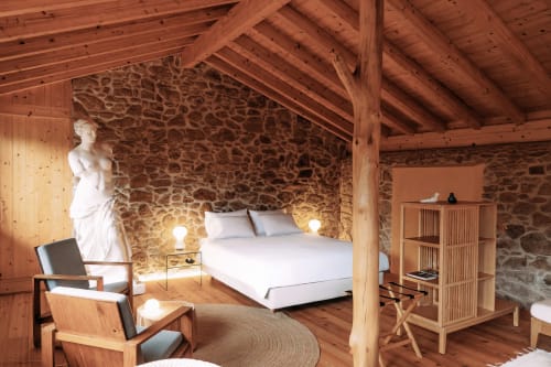 Quarto rústico na Quinta da Mata de Baixo com paredes de pedra, vigas de madeira, cama branca e área de estar aconchegante
