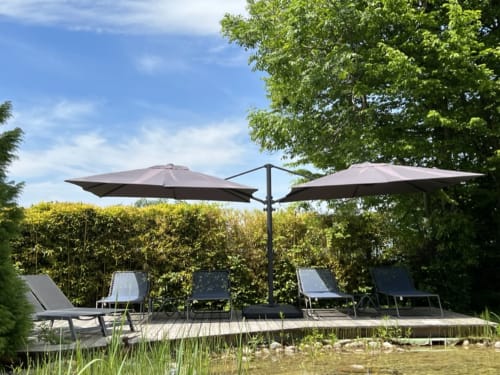 Waterfront patio at La Jument Verte with lounge chairs, double umbrellas, and wooden deck overlooking pond in Southern France