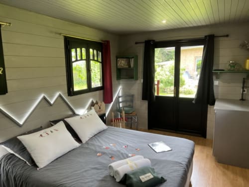 Modern bedroom at La Jument Verte B&B in Southern France with double bed, neon headlight, and glass doors opening to garden