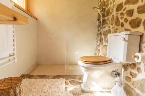 Rustic bathroom at Quinta da Mata de Baixo with stone walls, white toilet with wooden seat, shower, and natural lighting