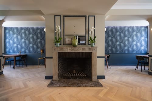 Le hall de L'Ode à Pierre à Dax avec cheminée, panneaux bleus à motifs, mobilier contemporain et parquet en chevrons