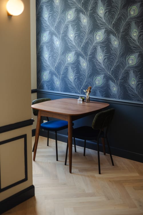 Coin repas contemporain à L'Ode à Pierre Dax avec table en bois, chaises rembourrées bleues et papier peint à motifs de plumes de paon
