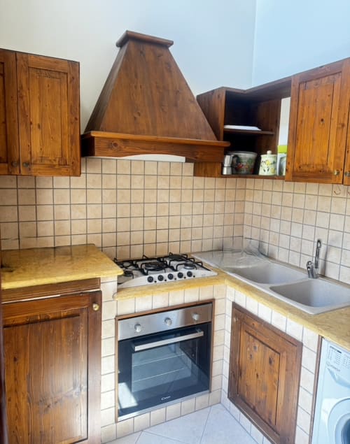 Cucina rustica con mobili in legno, fornello a gas, forno incassato e rivestimento in piastrelle bianche nell'appartamento HABITARE Lecce