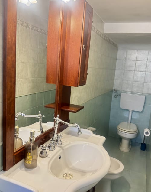 Elegante bagno dell'appartamento HABITARE Lecce con lavabo bianco, rubinetteria vintage, piastrelle verdi e mobiletto con specchio in legno