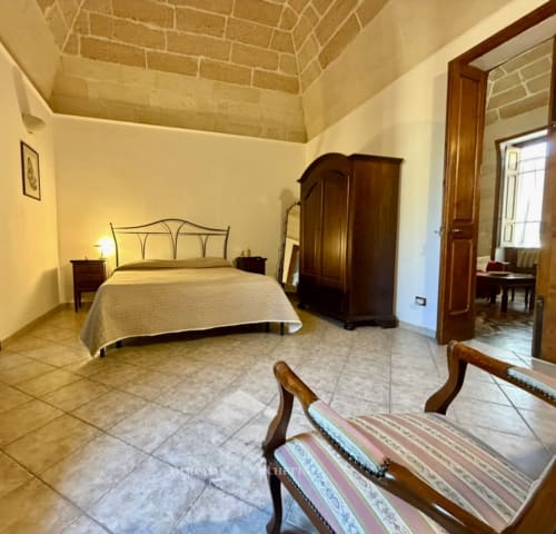 Spacious bedroom at HABITARE Lecce & Salento B&B with wrought iron bed, wooden wardrobe, and terracotta tile flooring in