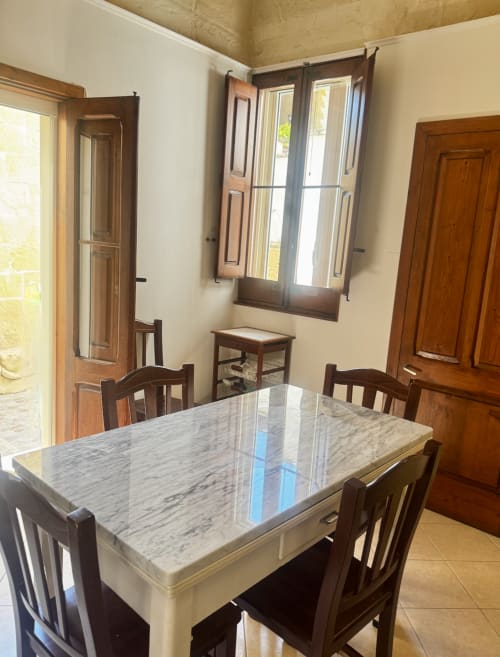 Bright dining room at HABITARE Lecce with marble table, wooden chairs, and traditional doors in Salento