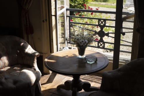 Élégant salon du Château de Vaux Morvan avec table ronde noire, fauteuils rembourrés et vue sur le jardin