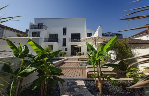 Cour de la boutique-hôtel L'Ode à Pierre à Dax avec architecture blanche moderne, terrasse en bois, piscine et plantes tropicales