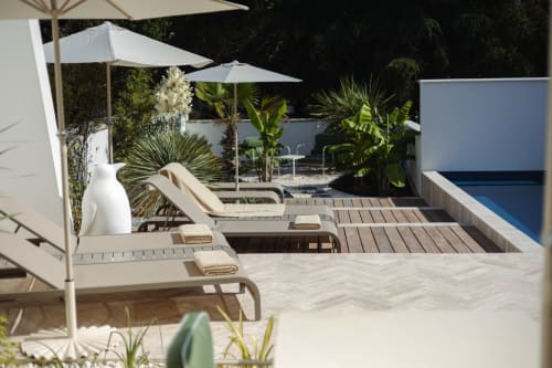 La terrasse piscine de L'Ode à Pierre à Dax avec transats, parasols blancs et plantes tropicales