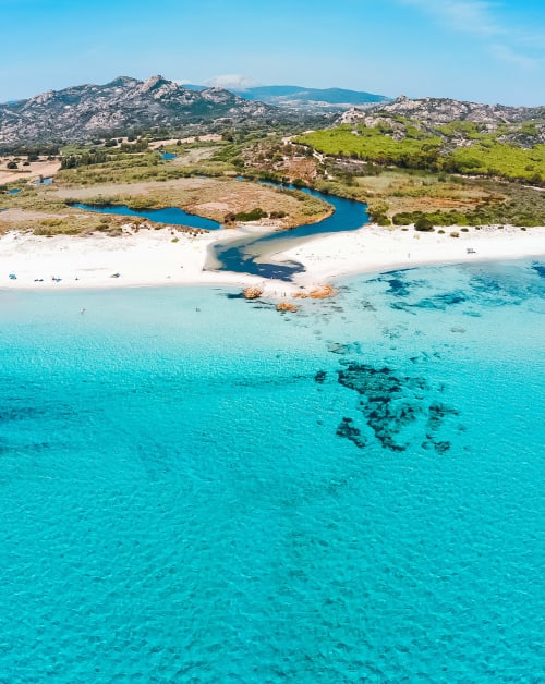 Acque turchesi e spiaggia sabbiosa bianca vicino a Berchidda, Italia con montagne granitiche e insenatura fluviale blu